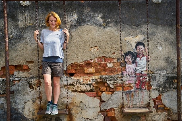 Usmiata žena stojí na hojdačke pri stene s grafitmi.jpg